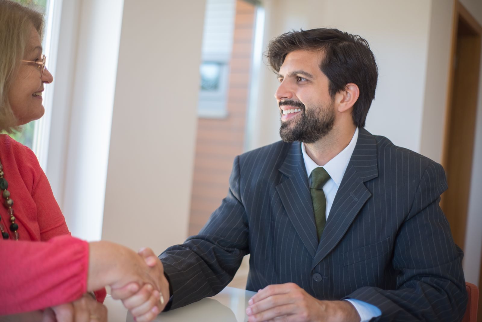 Travel advisor shaking hands with a smiling client across an office desk after selling cruises
