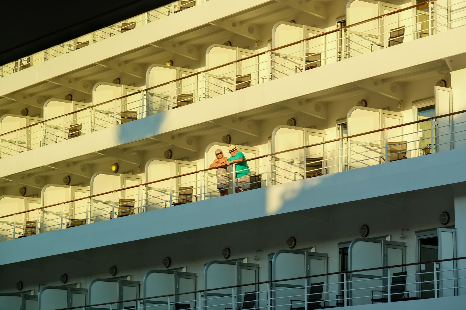 Rows of balcony cabins on the side of a cruise ship with guests standing outside