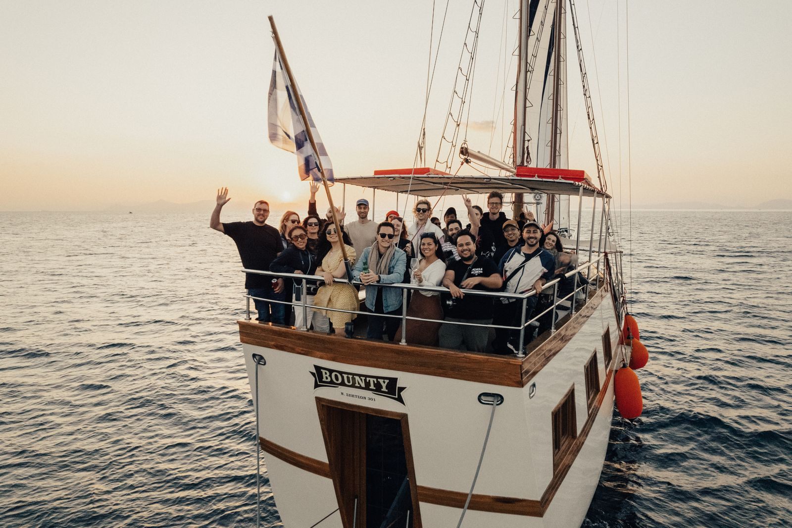 Large group of friends waving from the deck of a tall ship at sea, the kind of group that helps you sell more cruises