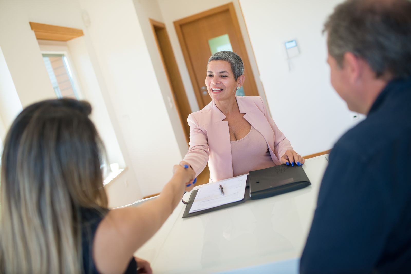 Advisor greeting a couple at her desk, ready to ask how to sell cruises as a travel agent should: questions first